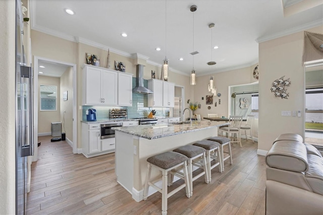 kitchen with light hardwood / wood-style flooring, wall chimney exhaust hood, white cabinetry, and pendant lighting