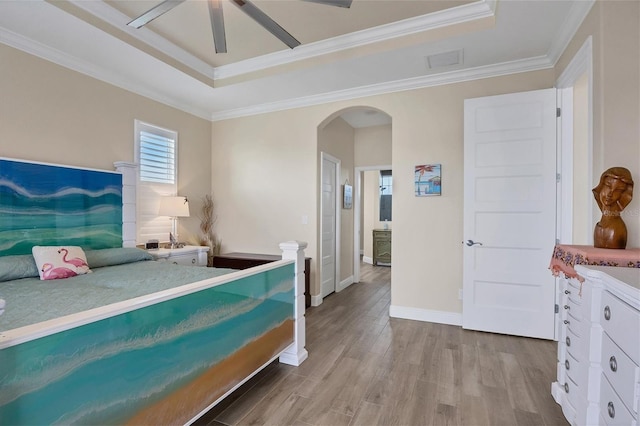 bedroom with light hardwood / wood-style flooring, ornamental molding, a tray ceiling, and ceiling fan