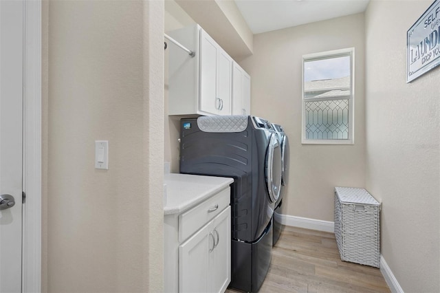 laundry area with washer and clothes dryer, light wood-type flooring, and cabinets