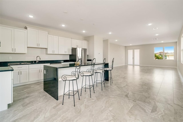 kitchen featuring sink, a kitchen island with sink, a kitchen breakfast bar, stainless steel refrigerator with ice dispenser, and white cabinets