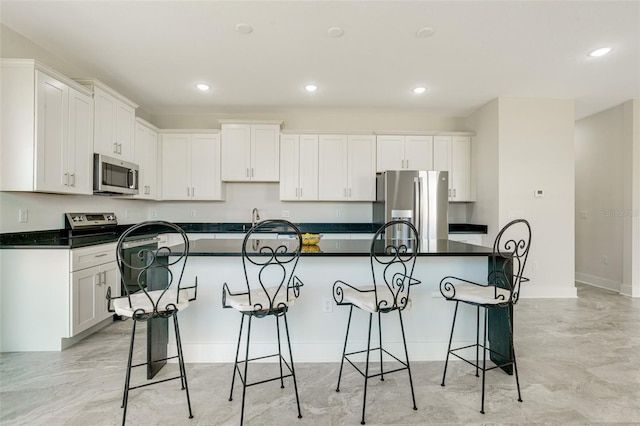 kitchen with white cabinetry, stainless steel appliances, a breakfast bar, and a kitchen island with sink