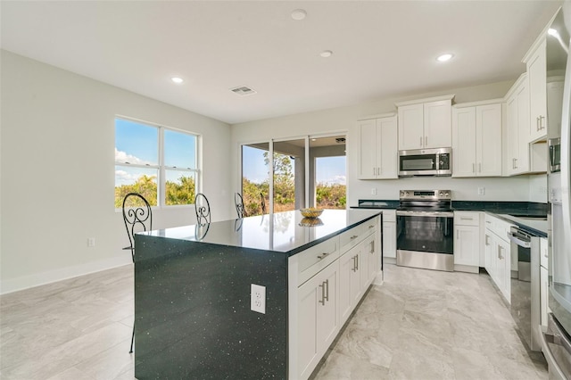 kitchen with a healthy amount of sunlight, a kitchen island, white cabinets, and appliances with stainless steel finishes