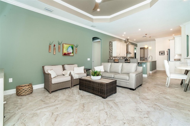 living room featuring a raised ceiling, ornamental molding, sink, and ceiling fan