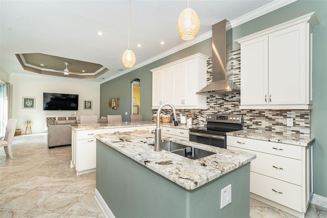 kitchen featuring hanging light fixtures, stainless steel electric stove, a kitchen island with sink, and wall chimney range hood