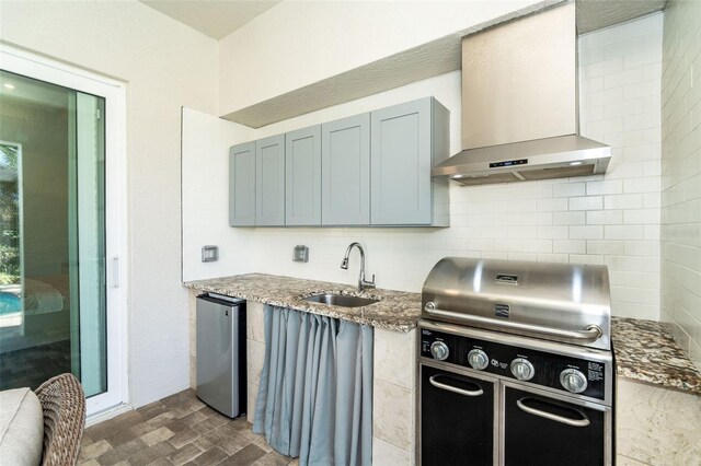 kitchen with stainless steel refrigerator, tasteful backsplash, sink, dark stone counters, and wall chimney range hood