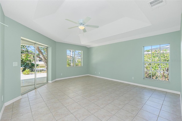 tiled empty room with a raised ceiling, ceiling fan, and a healthy amount of sunlight