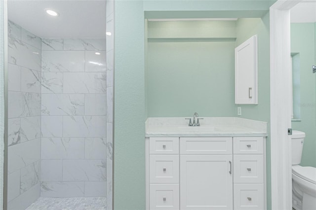 bathroom with a tile shower, vanity, and toilet