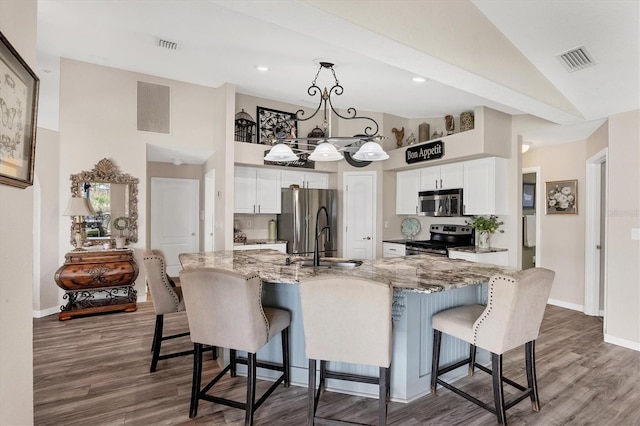 kitchen featuring stainless steel appliances, a breakfast bar area, white cabinetry, and light stone counters