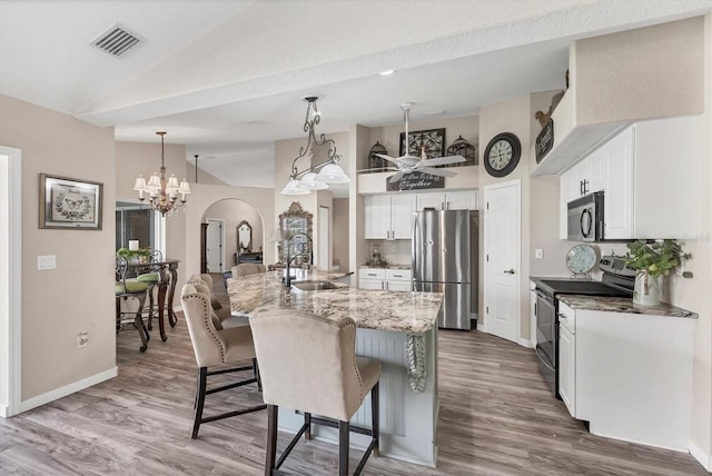 kitchen with vaulted ceiling, white cabinets, sink, appliances with stainless steel finishes, and decorative light fixtures