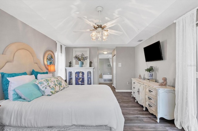 bedroom with dark wood-type flooring, connected bathroom, ceiling fan, and a raised ceiling