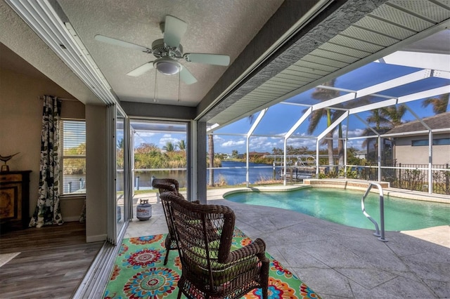 view of pool featuring ceiling fan, glass enclosure, a water view, and a patio area