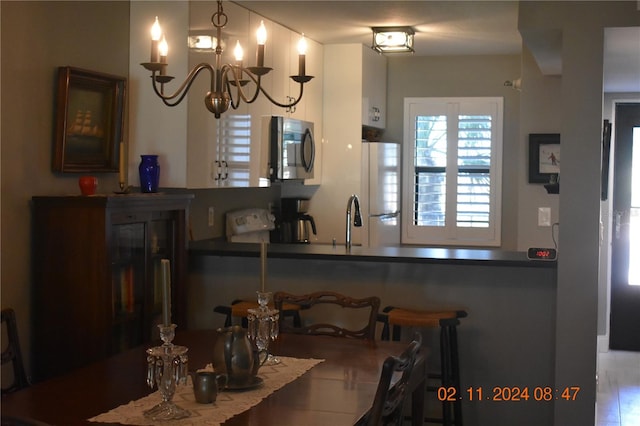 kitchen with a kitchen breakfast bar, white refrigerator, hanging light fixtures, kitchen peninsula, and a chandelier