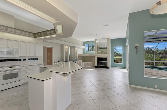 kitchen featuring white appliances, a kitchen island with sink, light tile patterned floors, and white cabinets