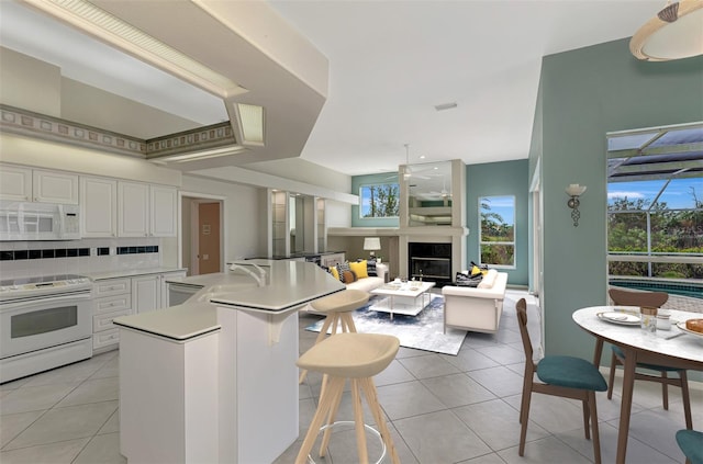 kitchen featuring light tile patterned flooring, a breakfast bar, ceiling fan, white appliances, and white cabinets