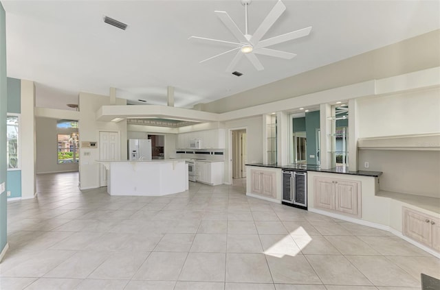 kitchen featuring light tile patterned flooring, ceiling fan, white appliances, beverage cooler, and a center island