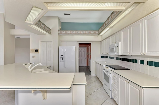 kitchen with backsplash, light tile patterned floors, sink, white cabinets, and white appliances