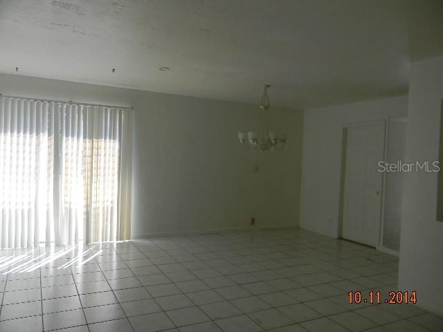 tiled empty room featuring an inviting chandelier