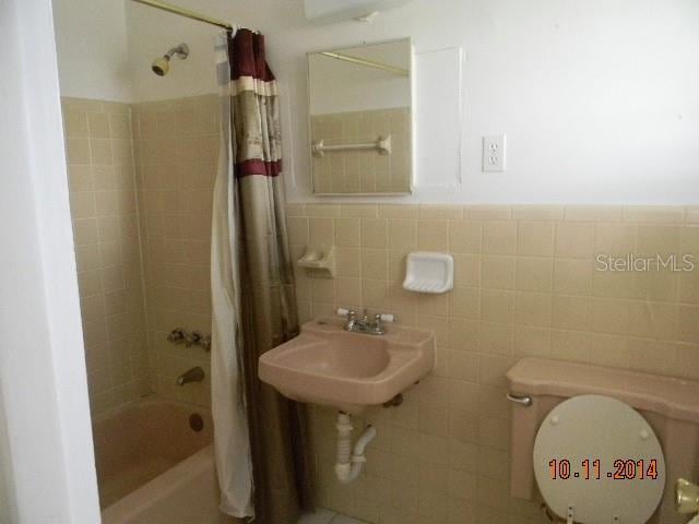 full bathroom with tile walls, shower / bath combination with curtain, toilet, and sink