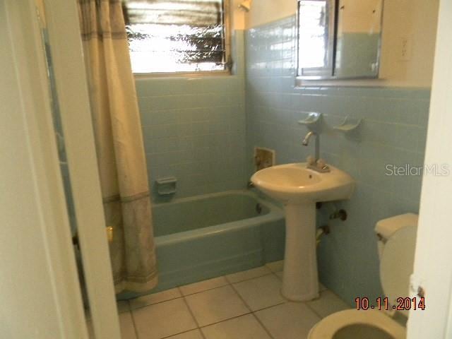 bathroom with tile walls, tile patterned floors, toilet, and shower / bathtub combination with curtain