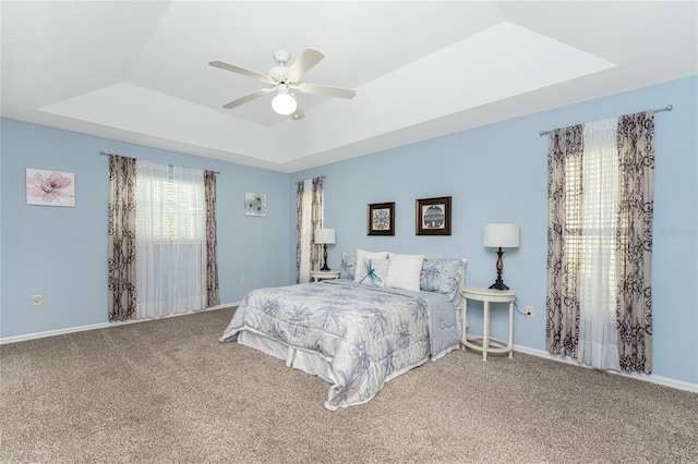 carpeted bedroom with ceiling fan and a raised ceiling