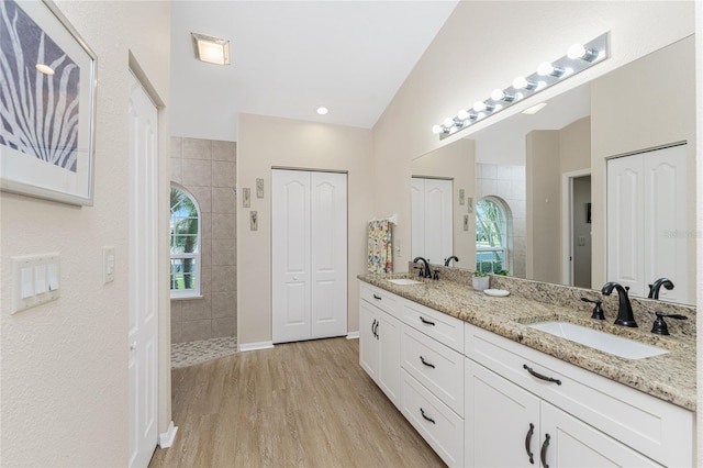 bathroom with vanity, lofted ceiling, a tile shower, and wood-type flooring