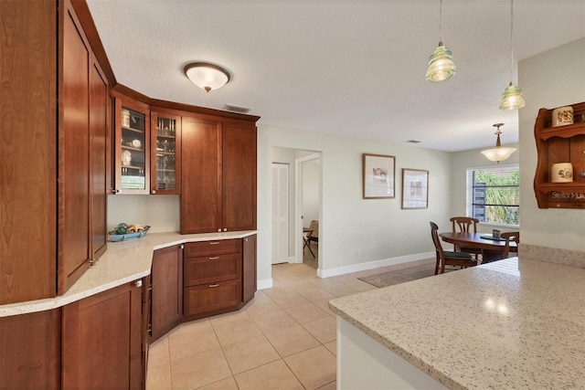 kitchen with a textured ceiling, light tile patterned flooring, pendant lighting, and light stone counters