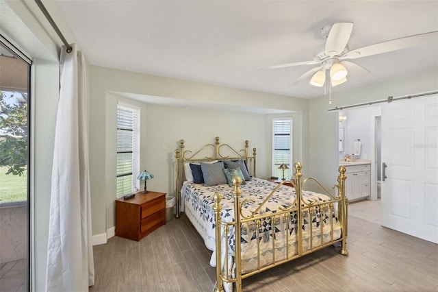 bedroom featuring light wood-type flooring, connected bathroom, ceiling fan, and a barn door