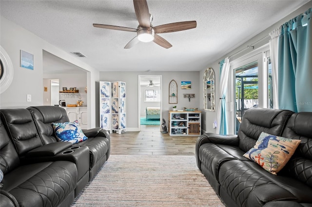 living room with light wood-type flooring, a textured ceiling, and ceiling fan