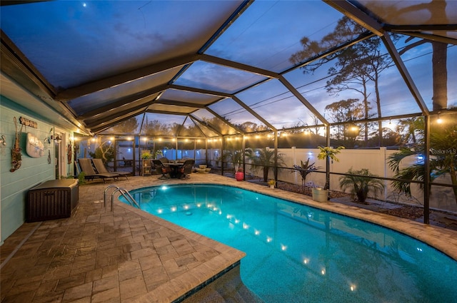 pool at dusk featuring glass enclosure and a patio area