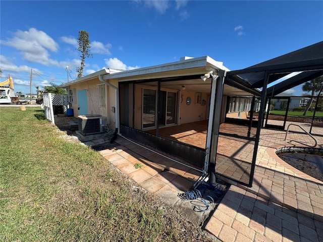 rear view of property featuring central AC unit, glass enclosure, a lawn, and a patio area