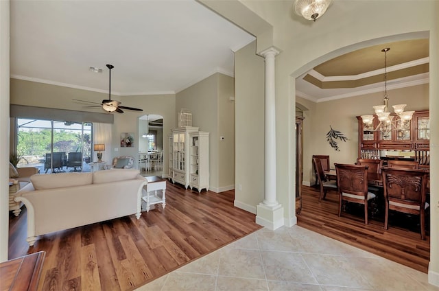 living room with crown molding, ceiling fan with notable chandelier, tile patterned floors, and ornate columns