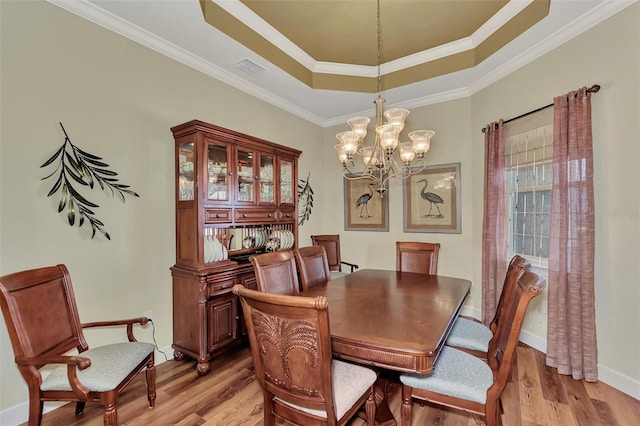 dining room with crown molding, a tray ceiling, light hardwood / wood-style floors, and a notable chandelier