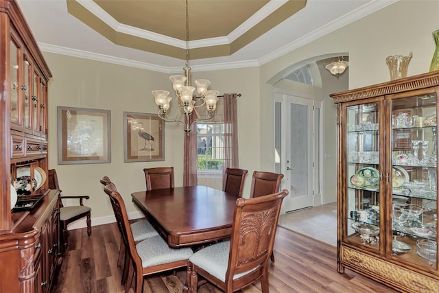 dining space with ornamental molding, wood-type flooring, a chandelier, and a tray ceiling