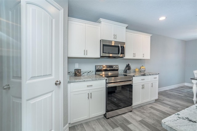 kitchen featuring white cabinets, appliances with stainless steel finishes, light hardwood / wood-style floors, and light stone counters