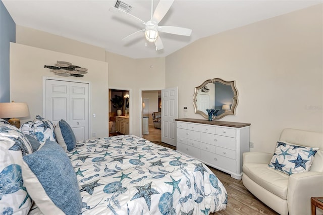 bedroom with a closet, connected bathroom, hardwood / wood-style floors, vaulted ceiling, and ceiling fan