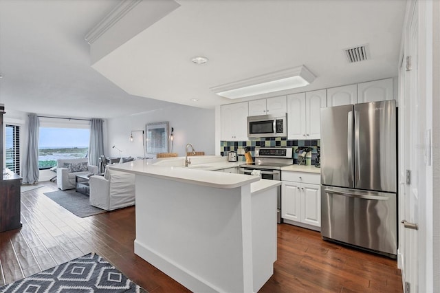 kitchen with white cabinets, dark hardwood / wood-style floors, appliances with stainless steel finishes, tasteful backsplash, and kitchen peninsula