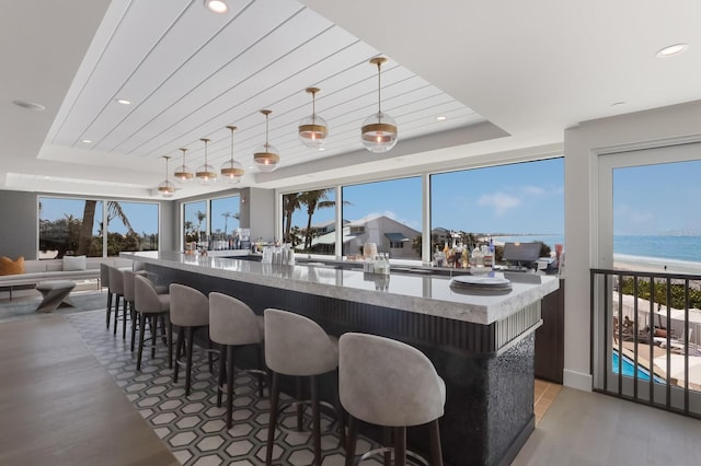 kitchen featuring a raised ceiling, decorative light fixtures, a water view, and plenty of natural light