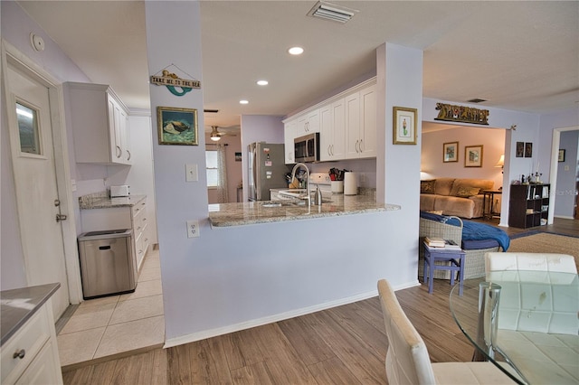 kitchen with light stone countertops, white cabinetry, kitchen peninsula, appliances with stainless steel finishes, and light wood-type flooring