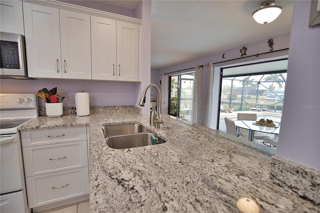 kitchen with light stone countertops, range, white cabinetry, and sink