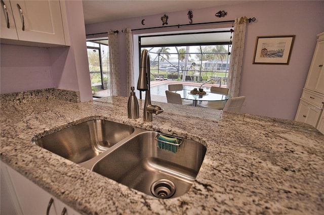 kitchen with light stone countertops, white cabinetry, and sink