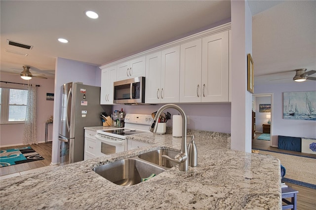 kitchen featuring kitchen peninsula, appliances with stainless steel finishes, light stone counters, sink, and white cabinets