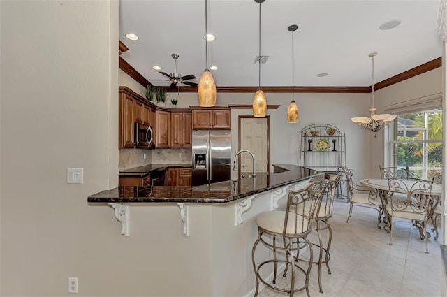 kitchen featuring stainless steel appliances, dark stone countertops, a breakfast bar area, hanging light fixtures, and decorative backsplash