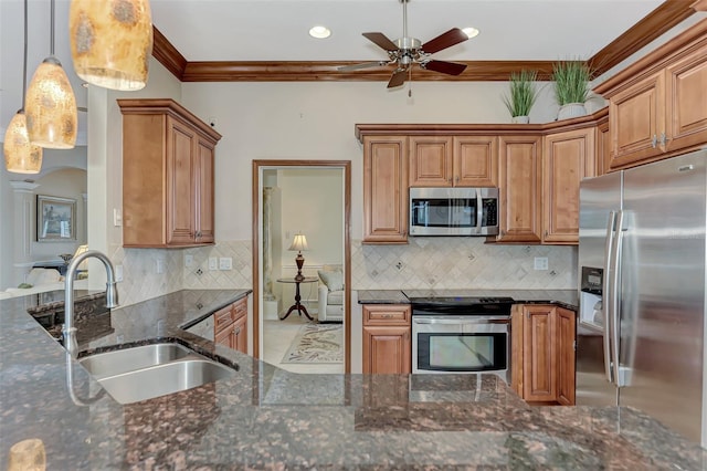 kitchen featuring crown molding, appliances with stainless steel finishes, hanging light fixtures, sink, and dark stone countertops