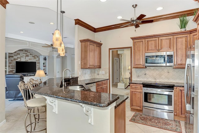 kitchen featuring stainless steel appliances, sink, ornamental molding, dark stone countertops, and decorative light fixtures