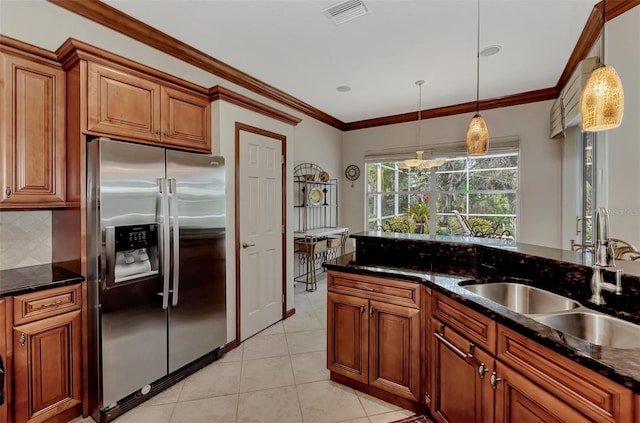 kitchen featuring dark stone countertops, hanging light fixtures, sink, and stainless steel fridge