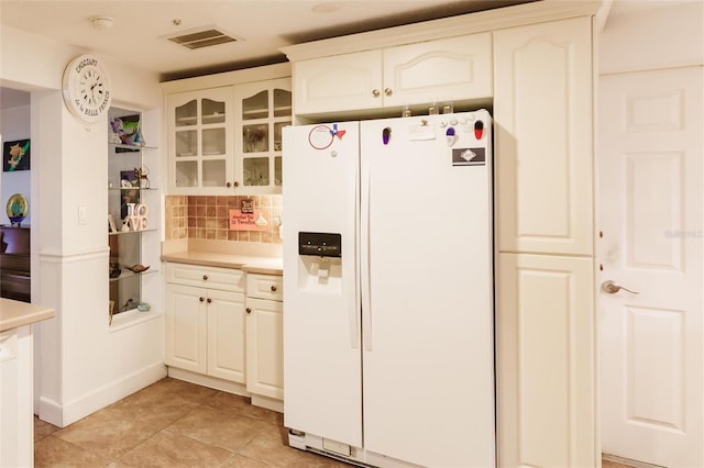 kitchen with backsplash, white cabinetry, light tile patterned floors, and white fridge with ice dispenser