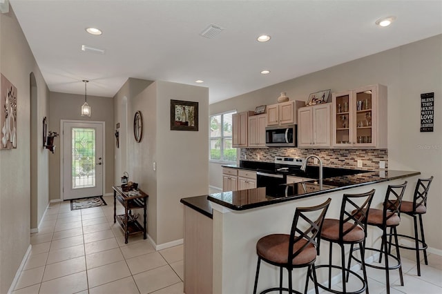 kitchen with stainless steel appliances, kitchen peninsula, a kitchen bar, light tile patterned floors, and decorative light fixtures