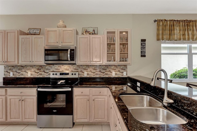 kitchen featuring stainless steel appliances, light tile patterned flooring, dark stone counters, and sink