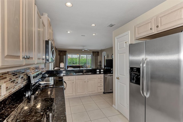 kitchen featuring stainless steel appliances, dark stone counters, light tile patterned floors, sink, and ceiling fan