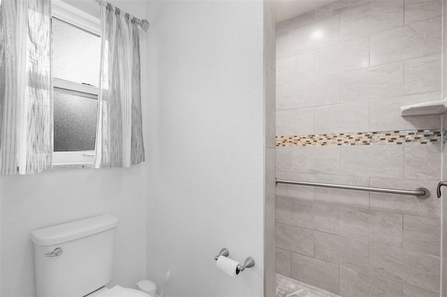 bathroom with a tile shower and toilet